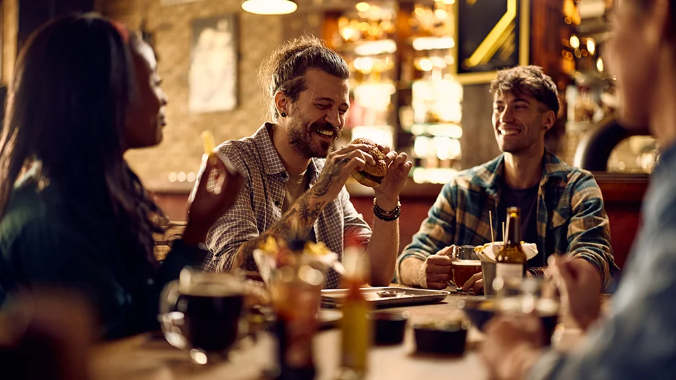 Cheerful man eating burger while gathering with friends in bar