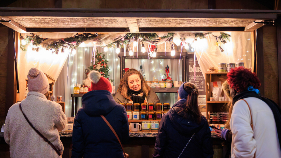 A market stand decorated with Christmas lights with several shoppers perusing.