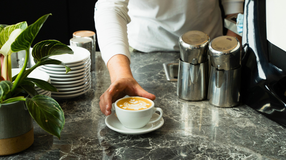 Barista presents a latte on a marble counter.