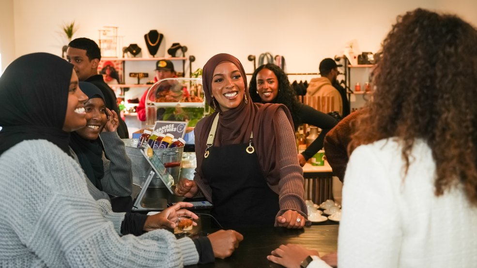 A woman smiles at customers from behind the counter of a cafe.