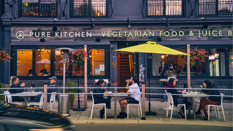 Street-side patio with people eating at bistro tables.