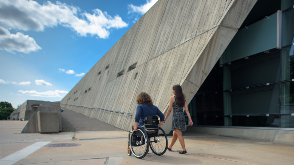 A person in a wheelchair and their friend enter a museum.