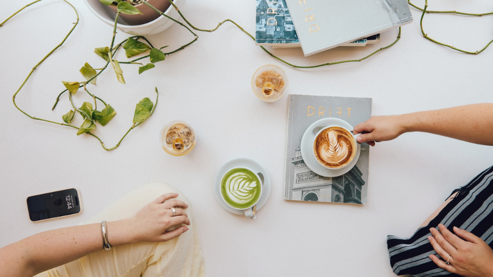 A café table with a latte, matcha and magazines.