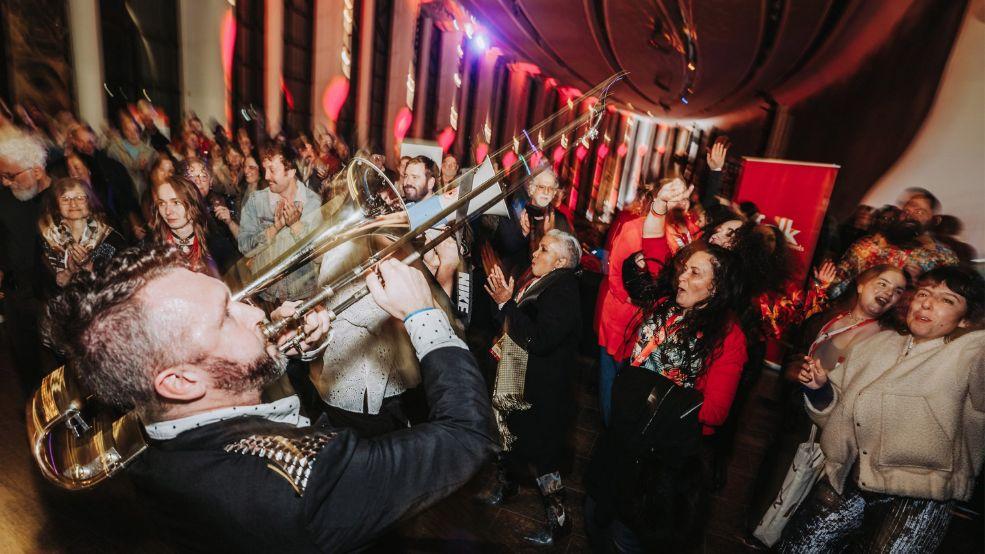 Trombone player plays instrument within a crowd of dancing and singing people at the Museum of History
