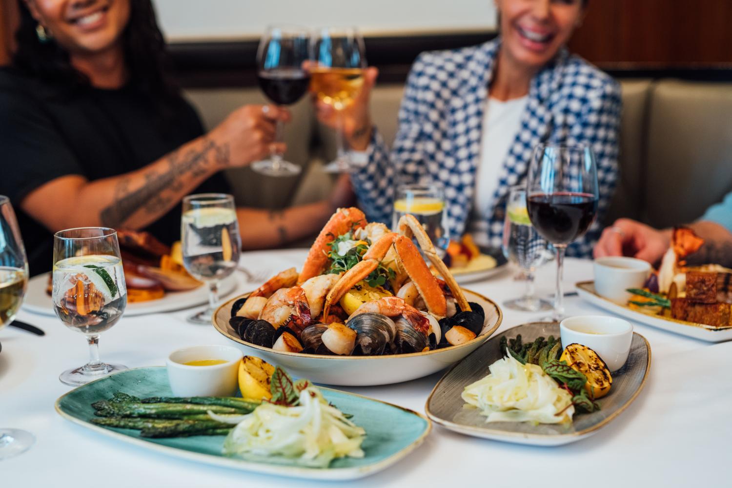 Two people clink their wine glasses over a full table of seafood and the fixings. 