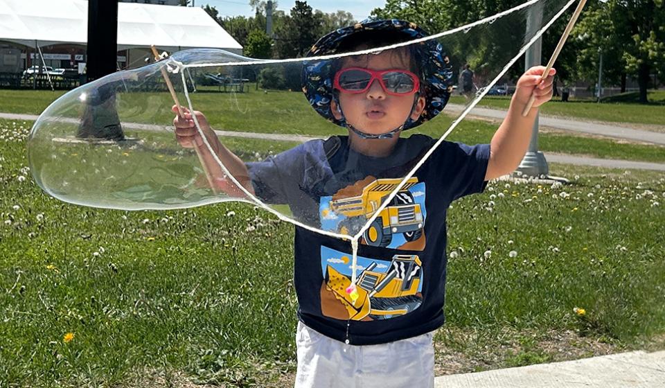 A young boy stands with a large bubble in his hands.