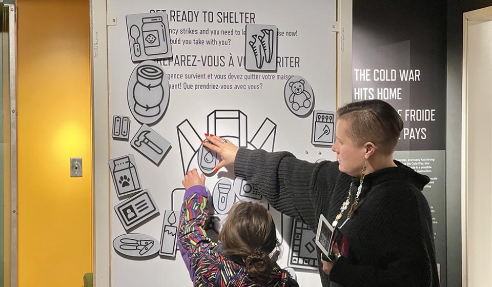 A child and parent move magnetic activity pieces around on a wall in a museum exhibition.