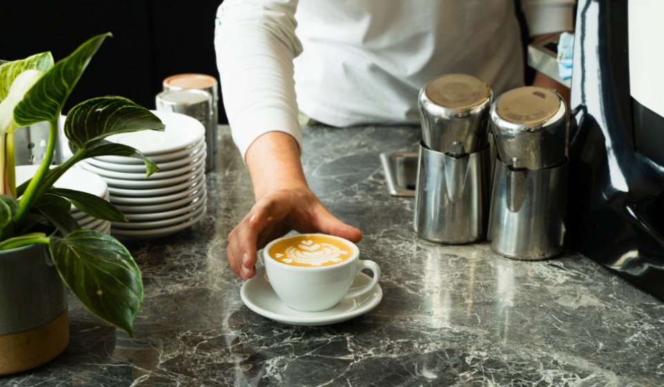 Barista presents a latte on a marble counter.