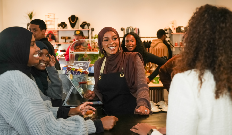 A woman smiles at customers from behind the counter of a cafe.
