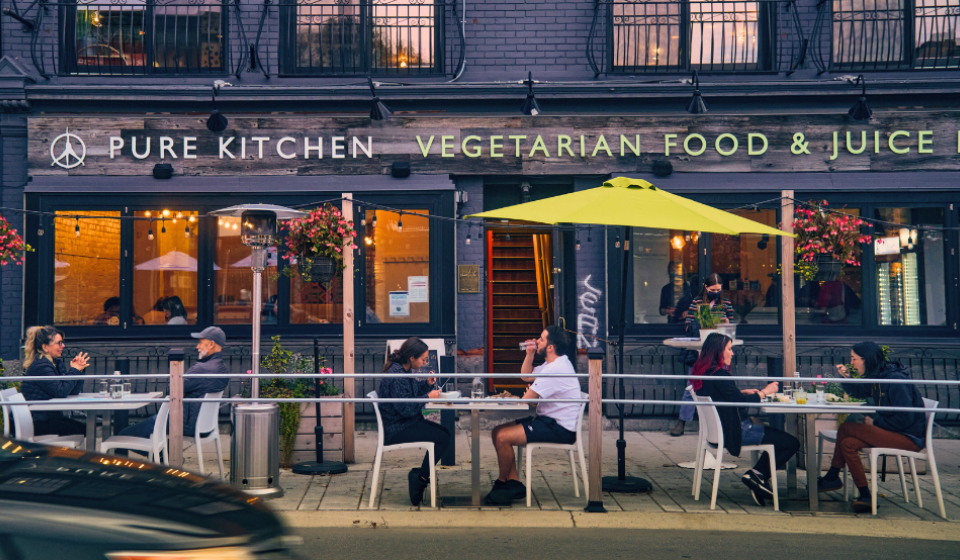 Street-side patio with people eating at bistro tables.