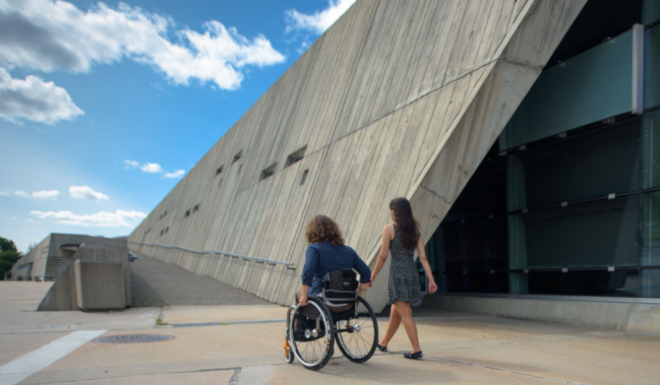 A person in a wheelchair and their friend enter a museum.