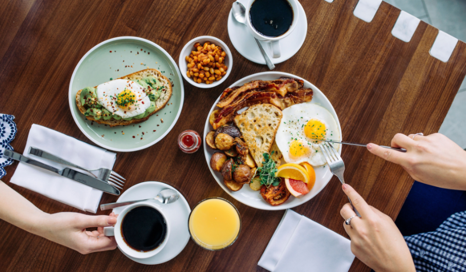 A wooden table set for two with breakfast dishes, black coffee