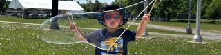 A young boy stands with a large bubble in his hands.