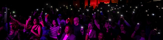 Crowd of people in a dark room with their phone's flashlight on