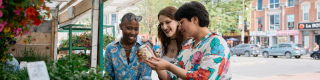 Three people looking at a jar at an outdoor market stand. 