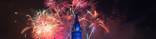 The Peace Tower is lit up in blue while red and pink fireworks explode behind it. 