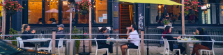 Street-side patio with people eating at bistro tables.
