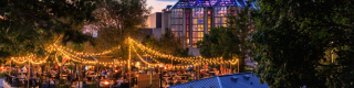 A bustling patio at sunset, lit with string lights in front of the facade of the National Gallery of Canada. 