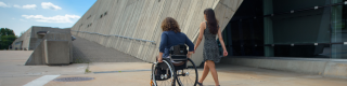 A person in a wheelchair and their friend enter a museum. 