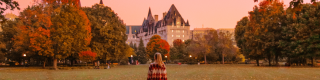 A woman walks in a park blanketed in fall leaves. 